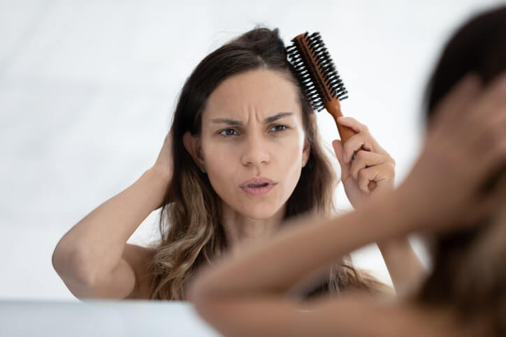 زن در مقابل آینه موی خودش را شانه می‌زند.