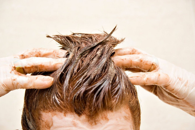 مرد جوان در حال رنگ کردن موهای خود به رنگ قهوه‌ای بلوطی